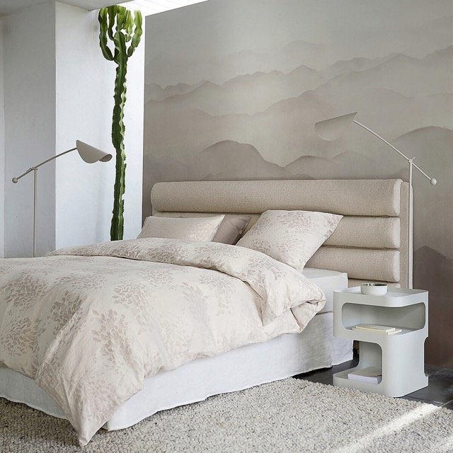 Chambre lumineuse avec tête de lit capitonnée beige, décoration minimaliste et ambiance apaisante.